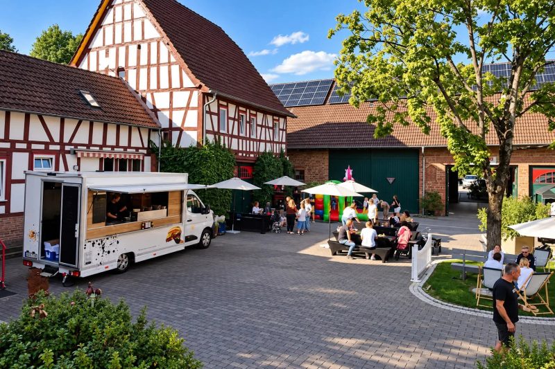 Blick über den Hof mit Gästen, Ständen und Sonnenschirmen beim Hoffest