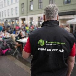 Mann i Evangeliesenteret-vest med påskriften «Ennå er det håp» foran en folkemengde