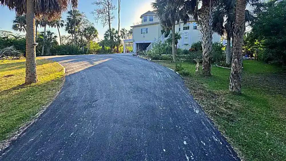 Finished residential asphalt millings driveway extension through tropical landscaping