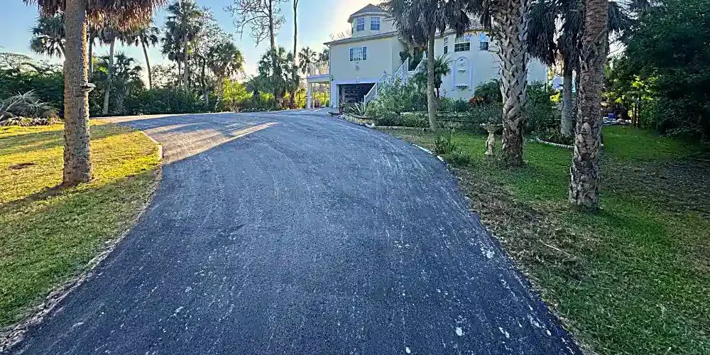 Finished residential asphalt millings driveway extension through tropical landscaping