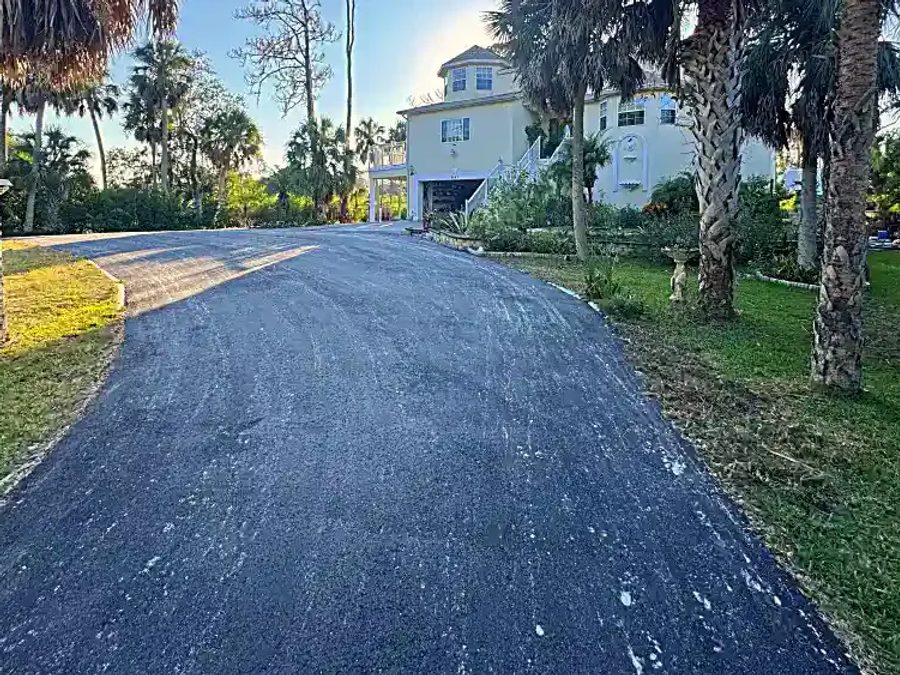 Finished residential asphalt millings driveway extension through tropical landscaping