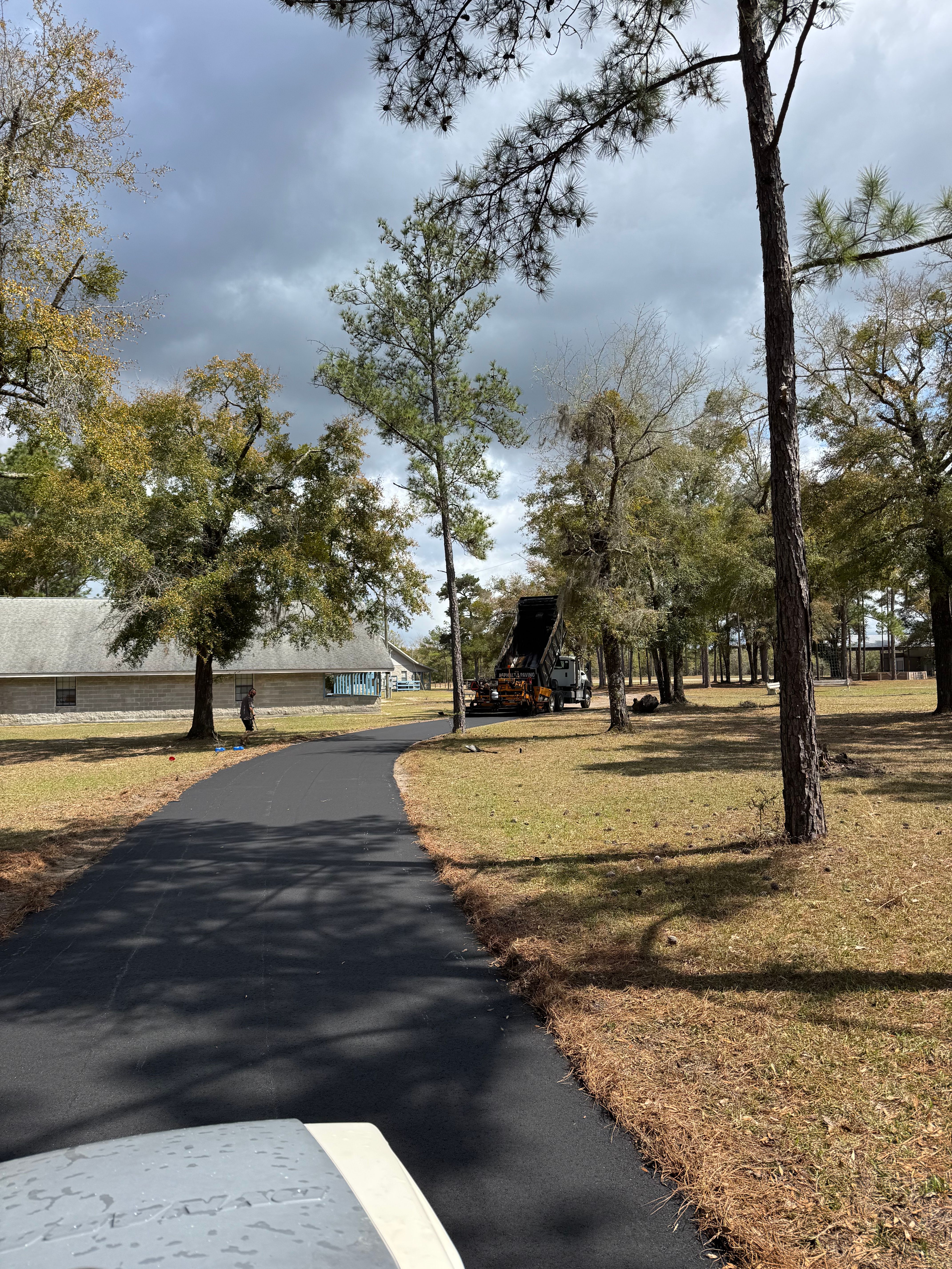 Completed black asphalt driveway through a wooded rural property
