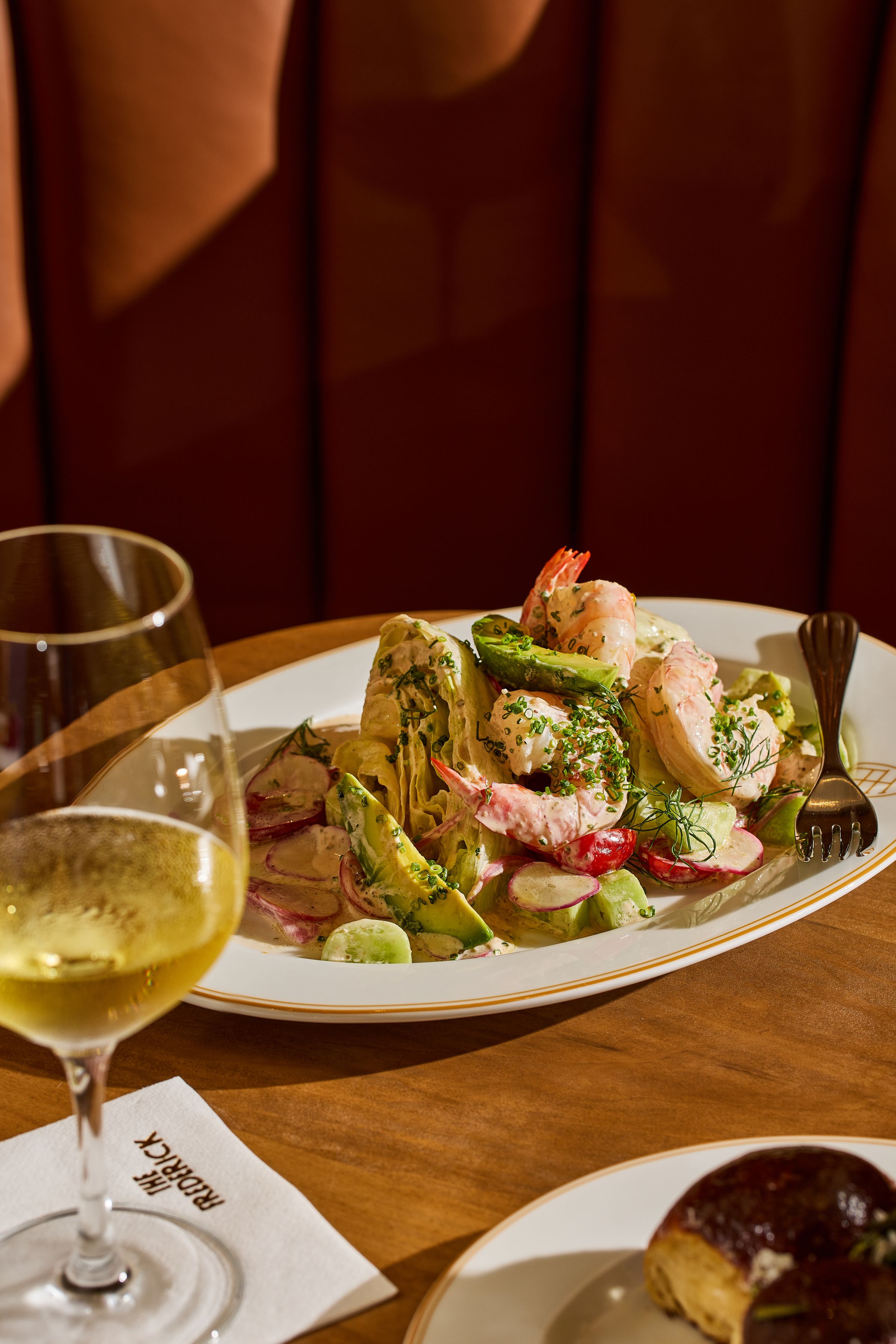 A chopped salad with prawns and a glass of white wine on top of a Frederick branded napkin.