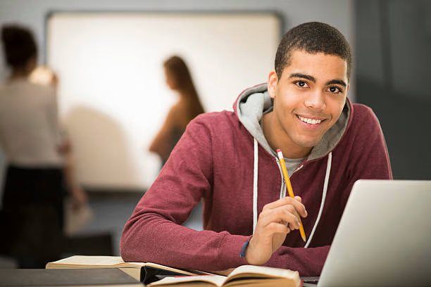 A young man smiling while working on a laptop
