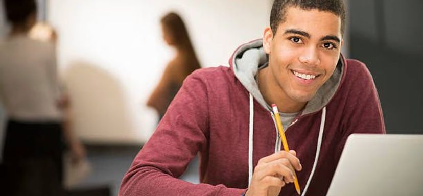 A young man smiling while working on a laptop
