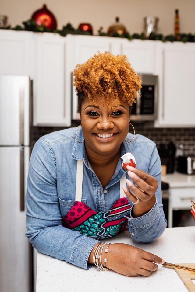 Julie Andrea smiling in her kitchen with a strawberry, wearing an apron