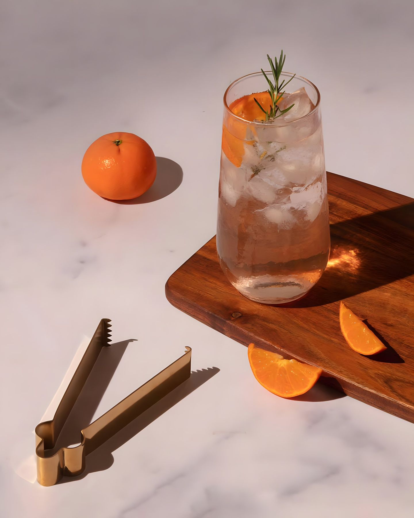 A tall glass with ice and an orange slice on a wooden board