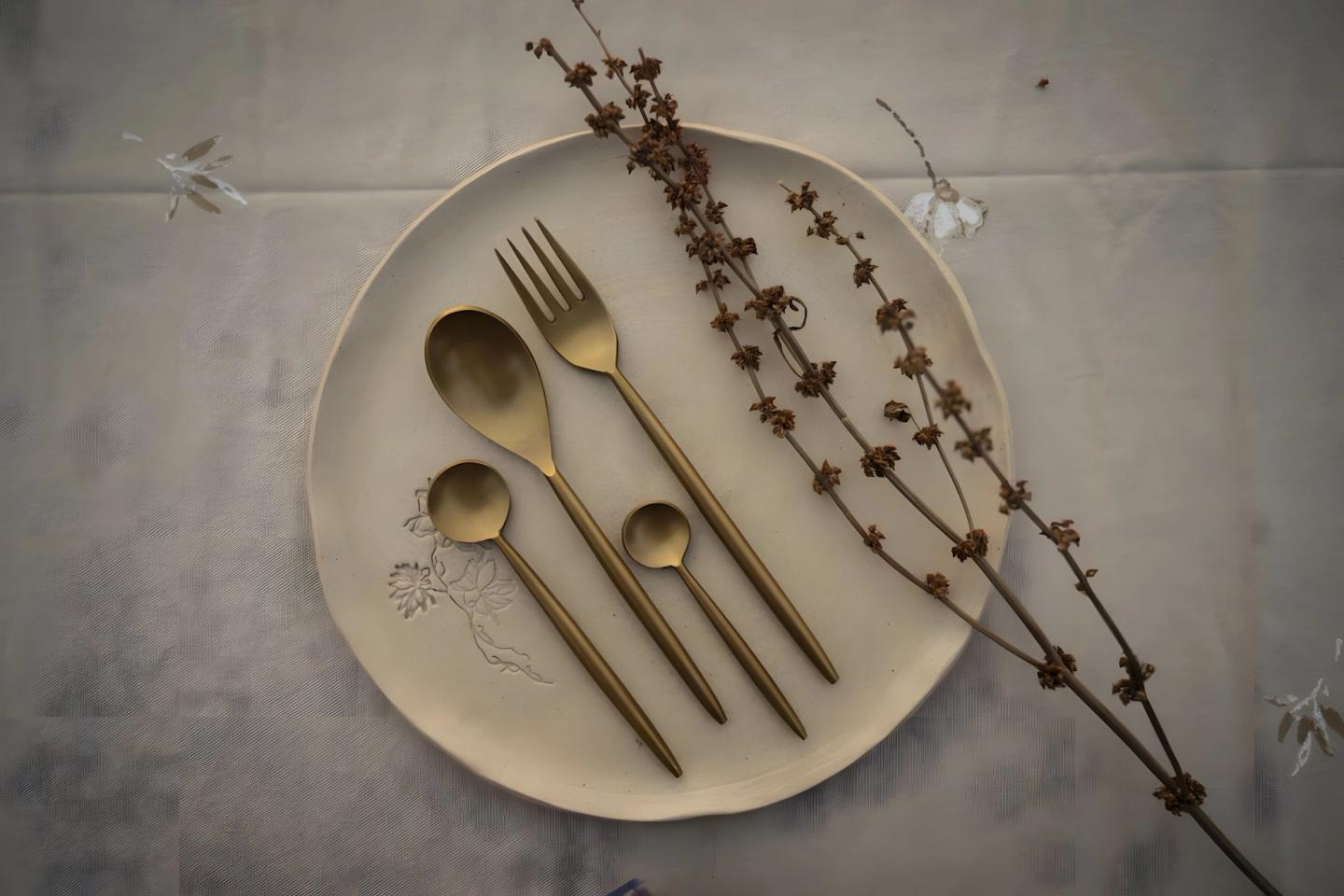 Brass cutlery and a sprig of dried flowers on a plate