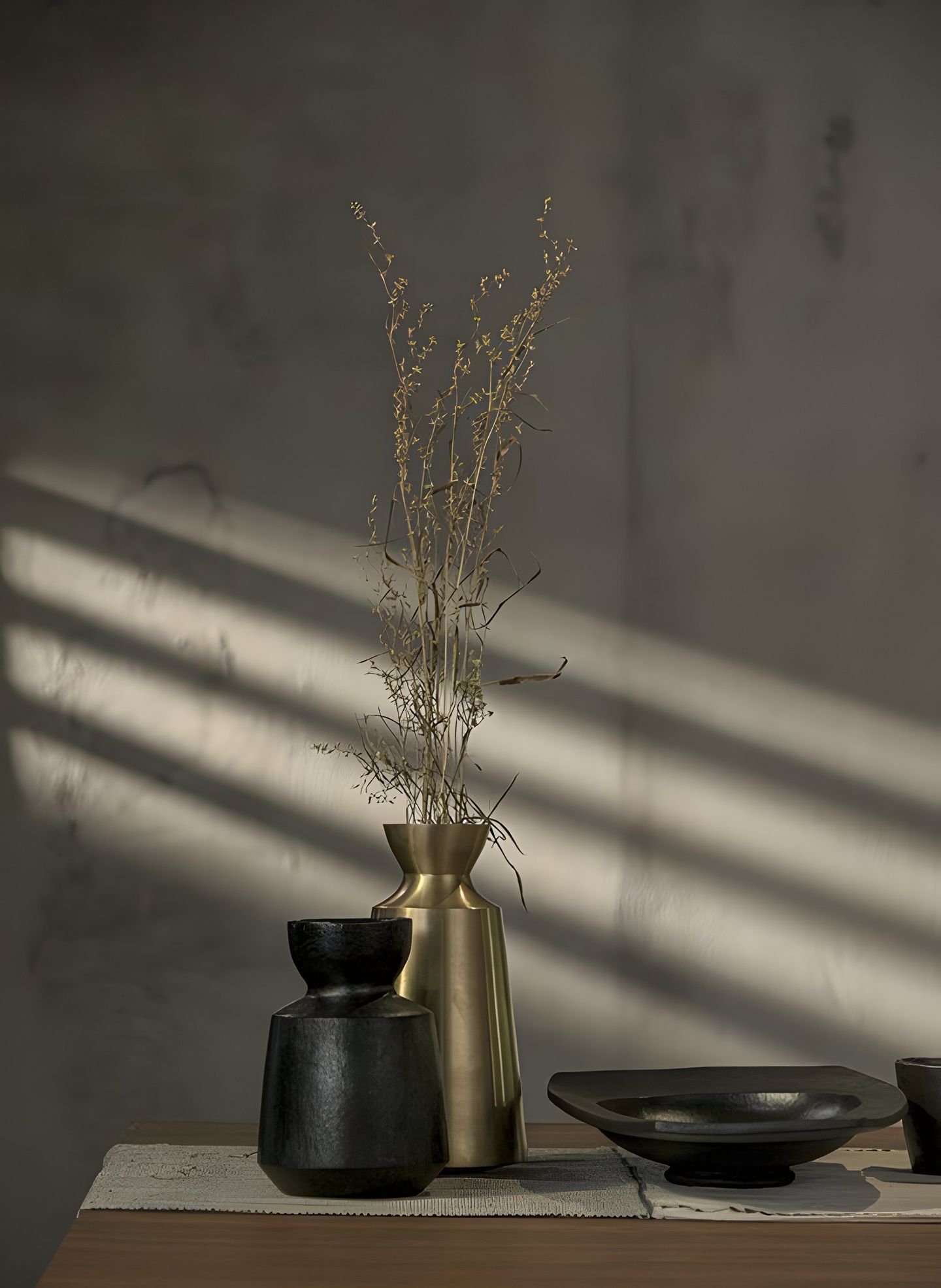 A dark vase with dried grass and a small bowl in striped light