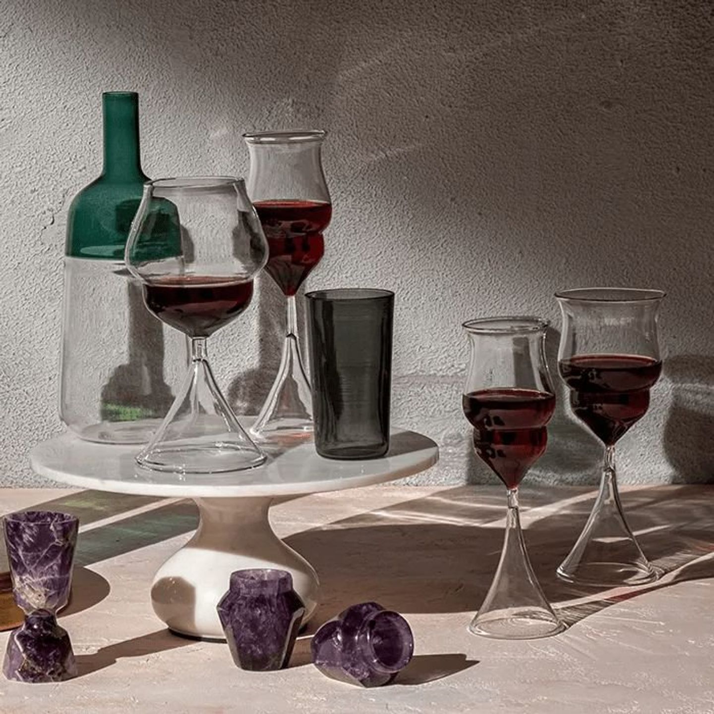 Wine glasses, a green bottle and amethyst on a marble stand