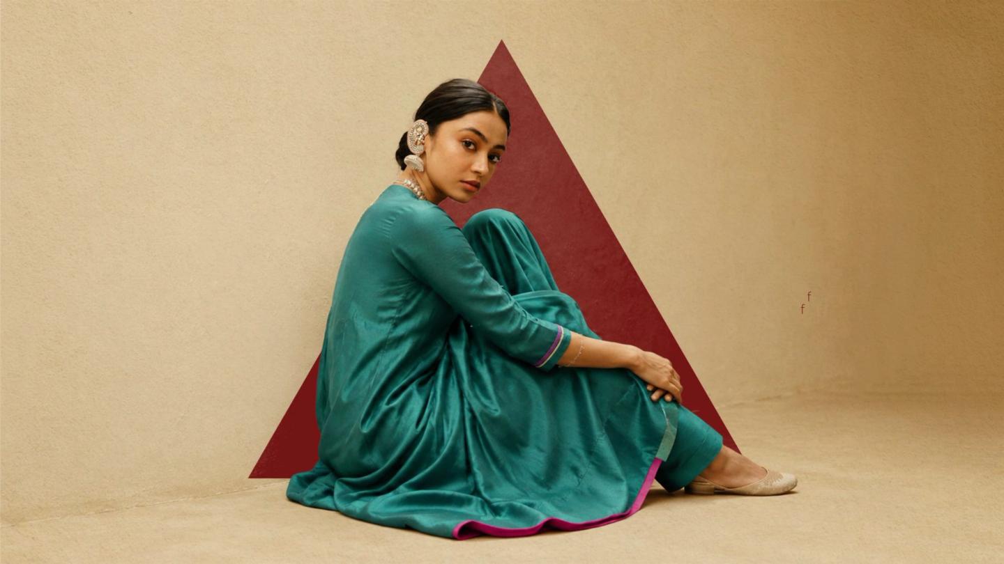 A model in a teal Lavira kurta set seated on sand in front of the brand’s crimson triangle
