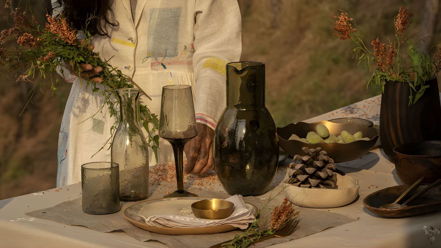 A woman holding dried flowers behind a laid table of smoked glass and brass