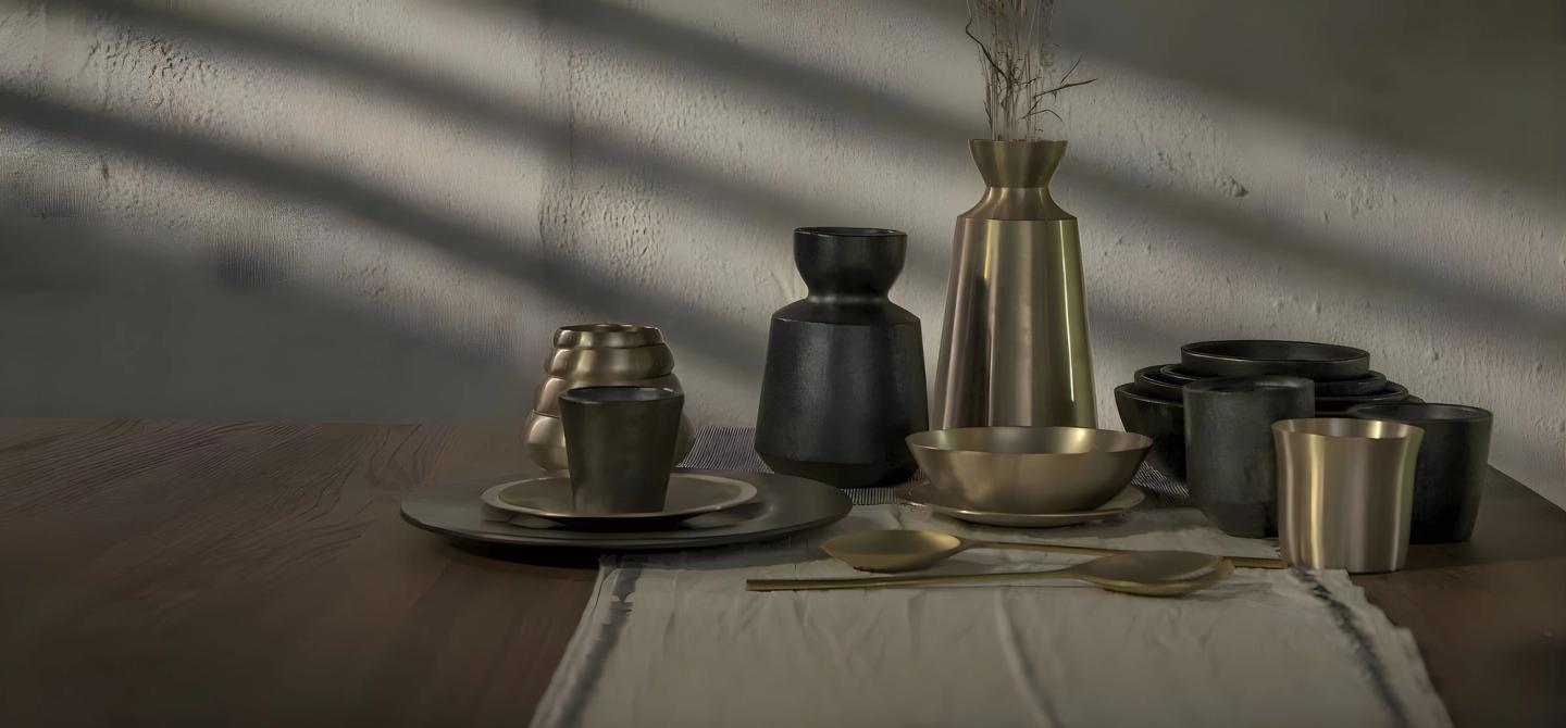 A table of dark metal vessels, bowls and plates in raking light