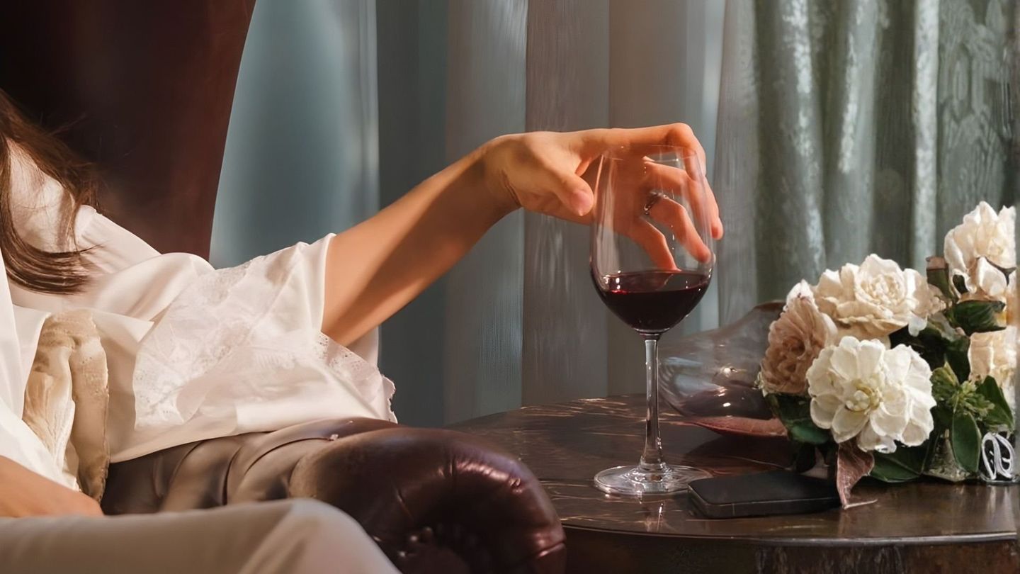 A hand reaching for a glass of red wine beside white flowers