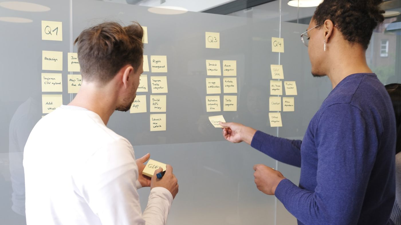 Deux personnes organisent des post-it sur un mur vitré