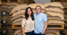 Carmen Castro and Joop Verbeek from Incafé with arms around each other posing in front of full brown sacks Carmen Castro and Joop Verbeek from Incafé with arms around each other posing in front of full brown sacks