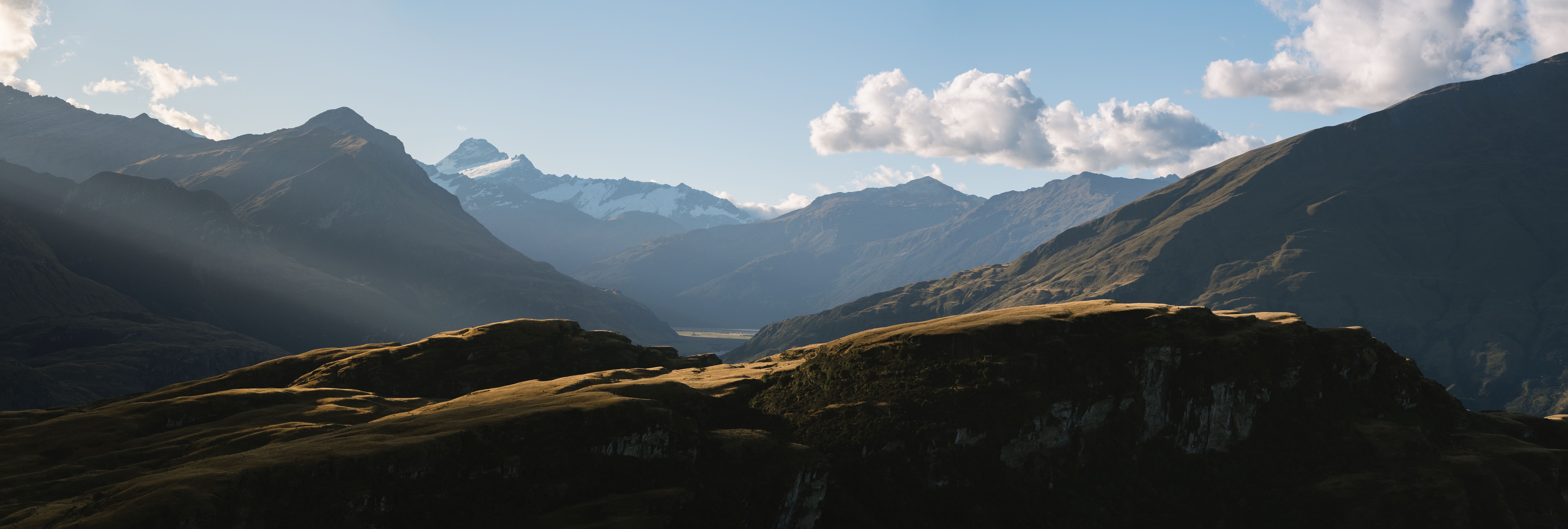 New Zealand rolling hill with snow capped mountain in the background and sun light shining through