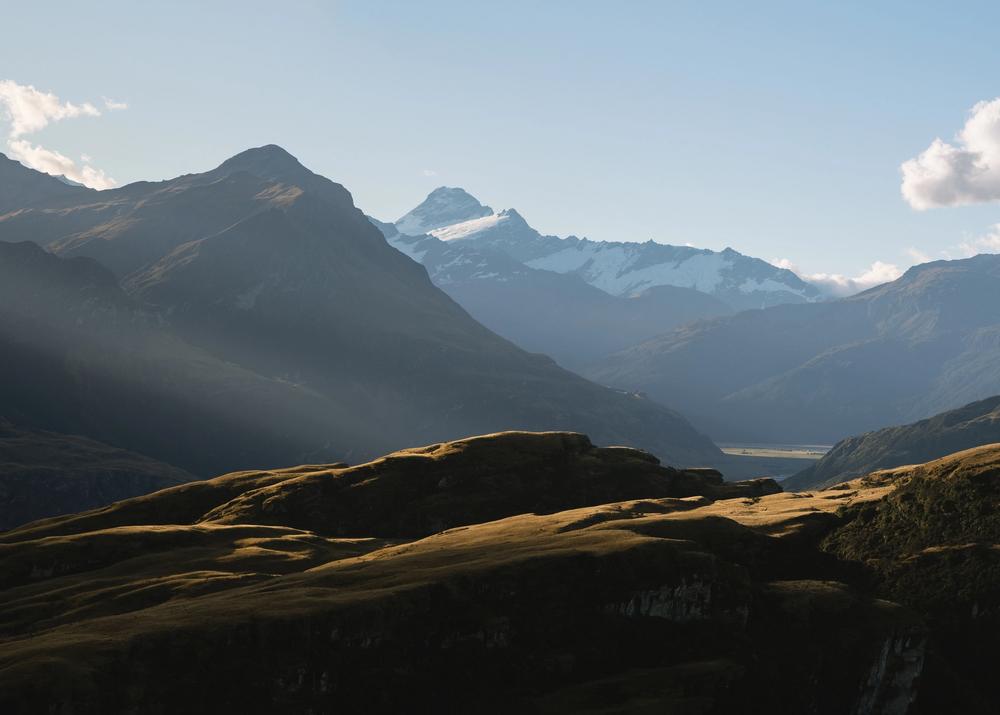New Zealand rolling hill with snow capped mountain in the background and sun light shining through New Zealand rolling hill with snow capped mountain in the background and sun light shining through