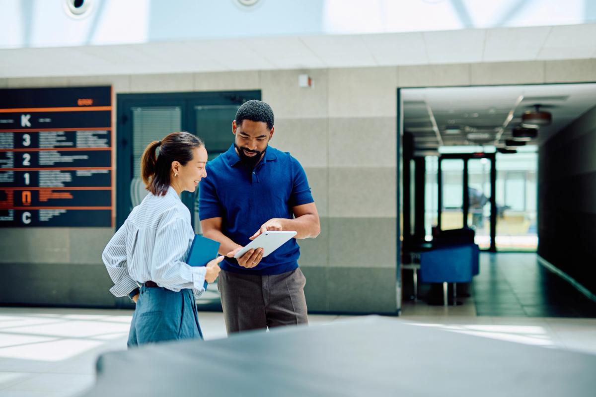 Man and woman looking at tablet on in corporate building Man and woman looking at tablet on in corporate building
