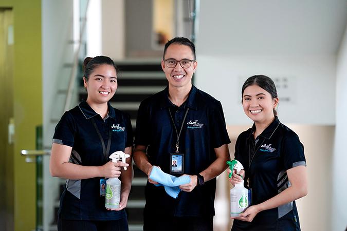 Three workers at Jani King smiling for photo holding cleaning products