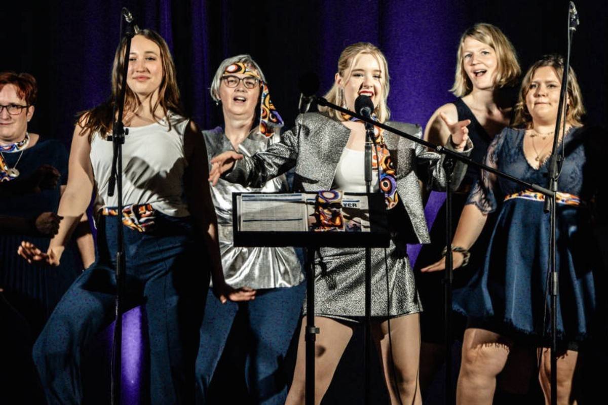 Sängerinnen des Showchors singen an Mikrofonständern vor blauem Bühnenvorhang