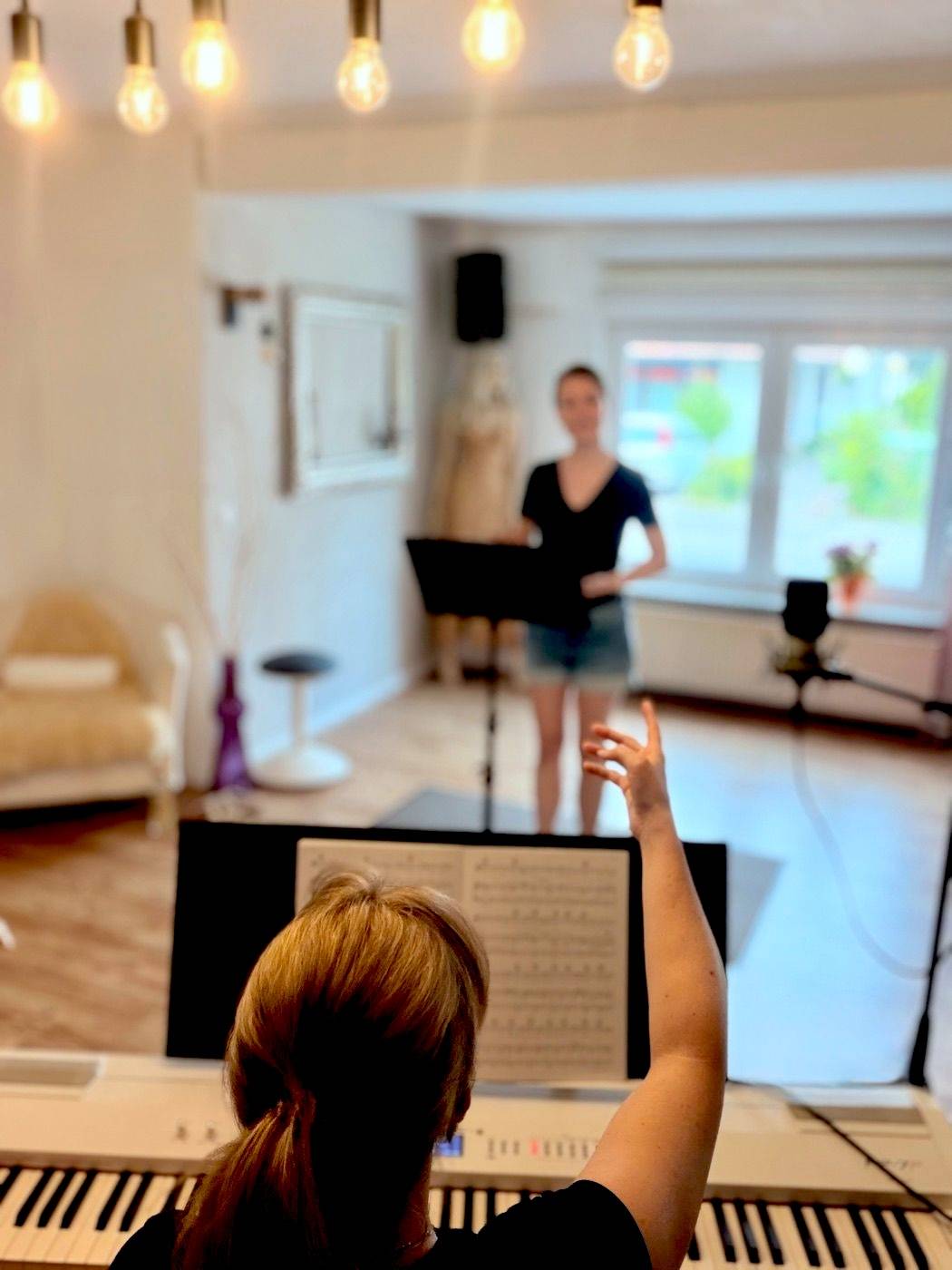 Blick vom Klavier in den Unterrichtsraum: Nina am Klavier, eine Schülerin singt am Notenständer