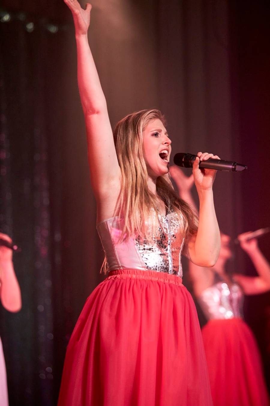 Nina Schromm singt mit erhobenem Arm auf der Bühne, im roten Tüllrock