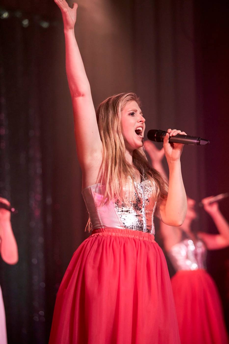 Nina singt mit erhobenem Arm auf der Bühne, im roten Tüllrock