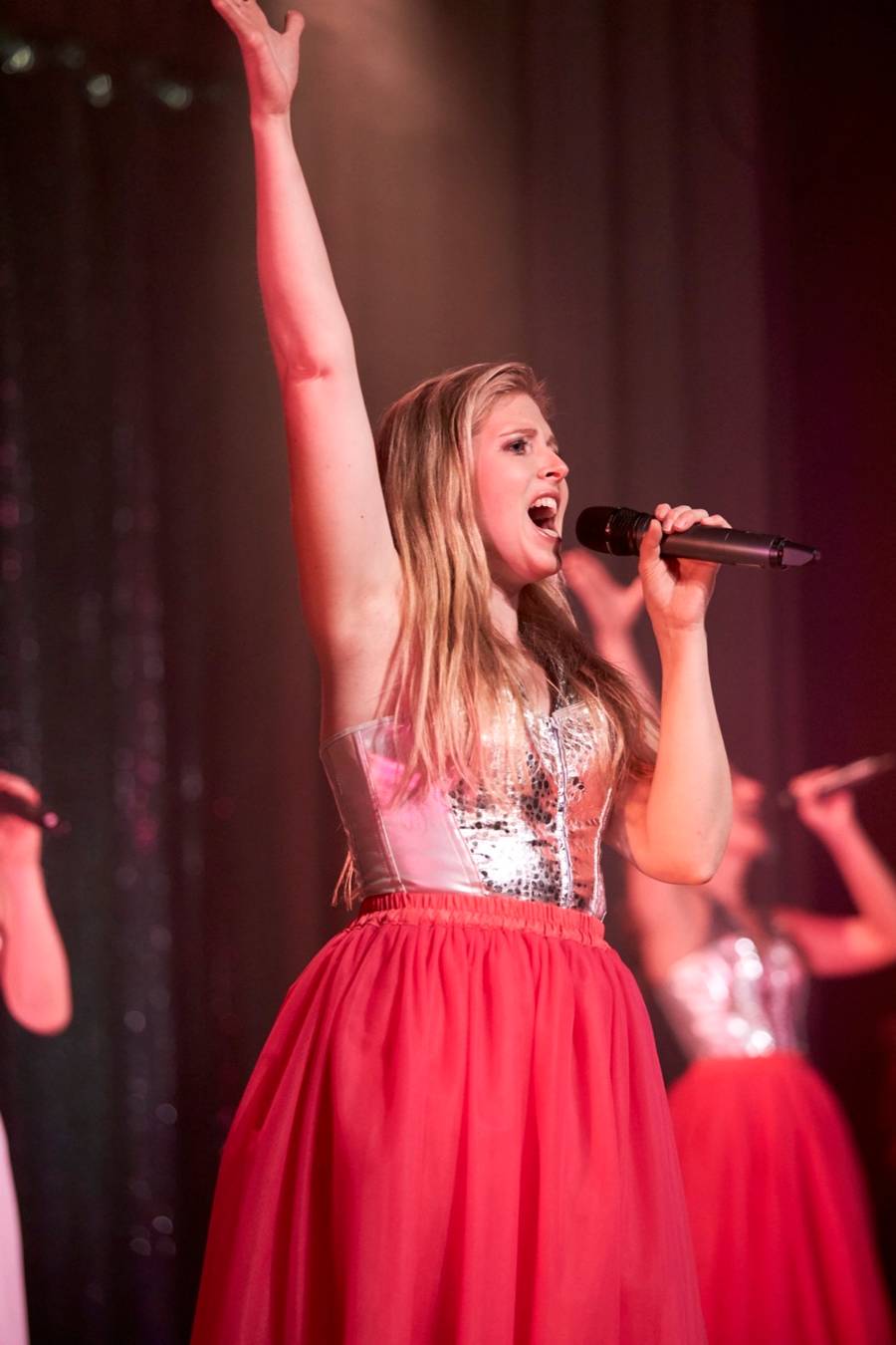 Nina Schromm singt mit erhobenem Arm auf der Bühne, im roten Tüllrock
