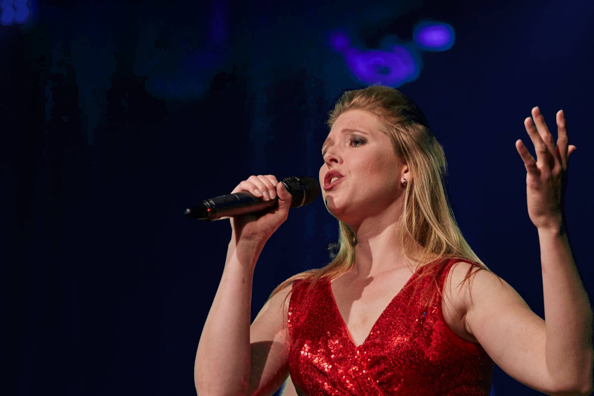 Nina Schromm singt im roten Paillettenkleid vor dunkelblauem Bühnenhintergrund