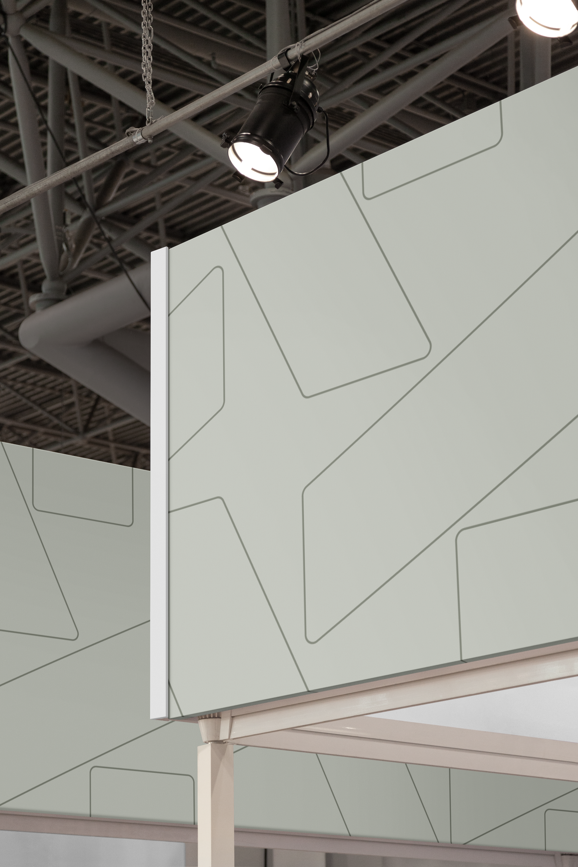 Close-up of an exhibition booth's sage-green wall printed with a thin-line geometric pattern, lit by a black stage spotlight mounted on overhead trusses.