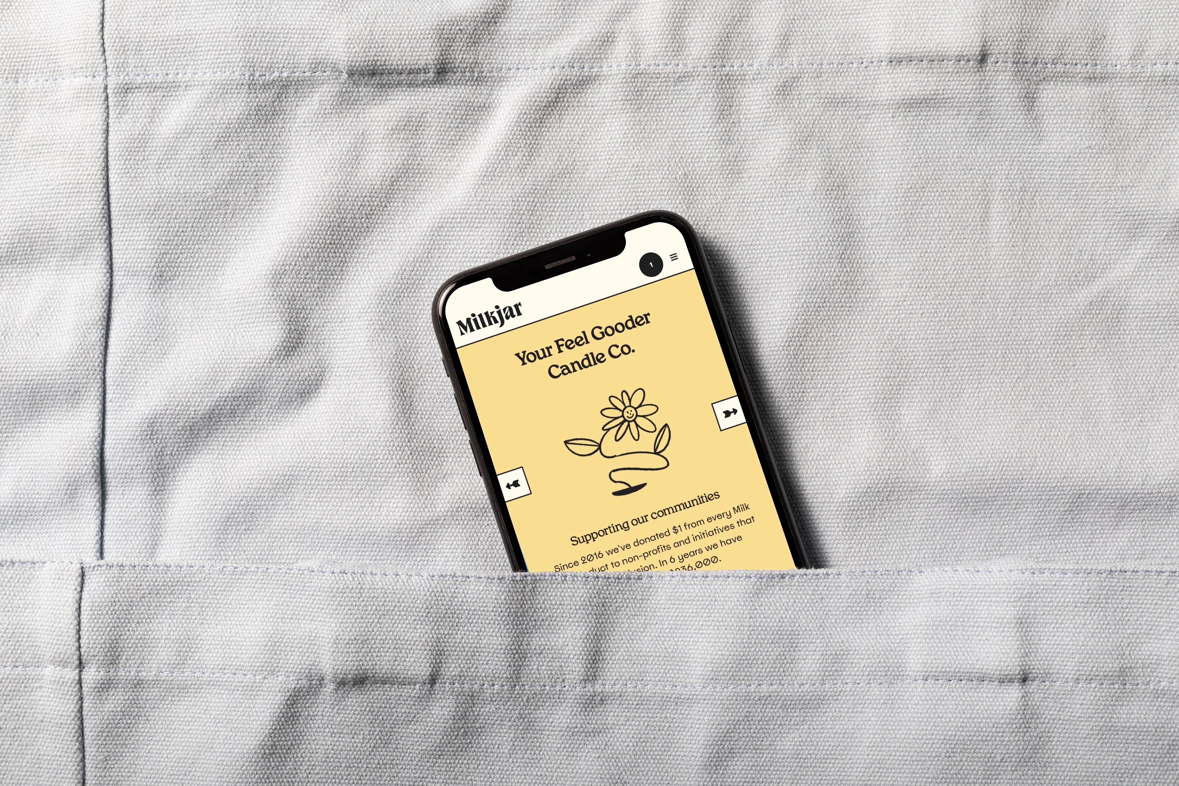 Smartphone tucked into a grey linen pocket displaying the yellow Milkjar website page reading 'Your Feel Gooder Candle Co.' with a line-drawn flower.