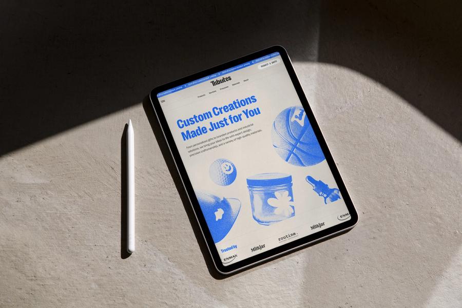 The Tributes website on a tablet beside a stylus, opening on the headline Custom Creations Made Just for You.