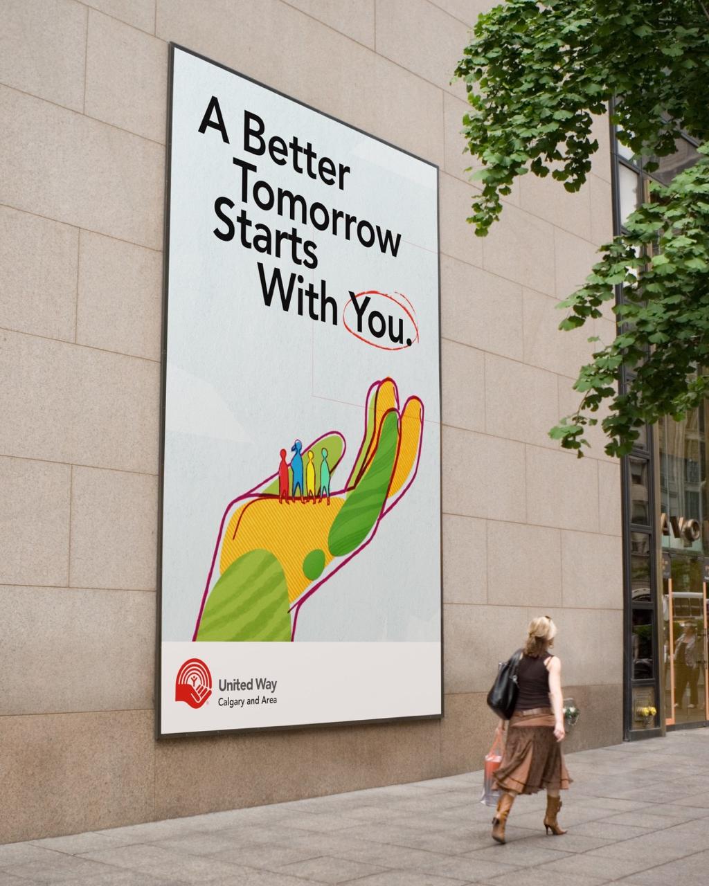 A billboard on a wall with the text "A Better Tomorrow Starts With You" and below the text is a large, colorful, illustrated hand with people standing in the palm.
