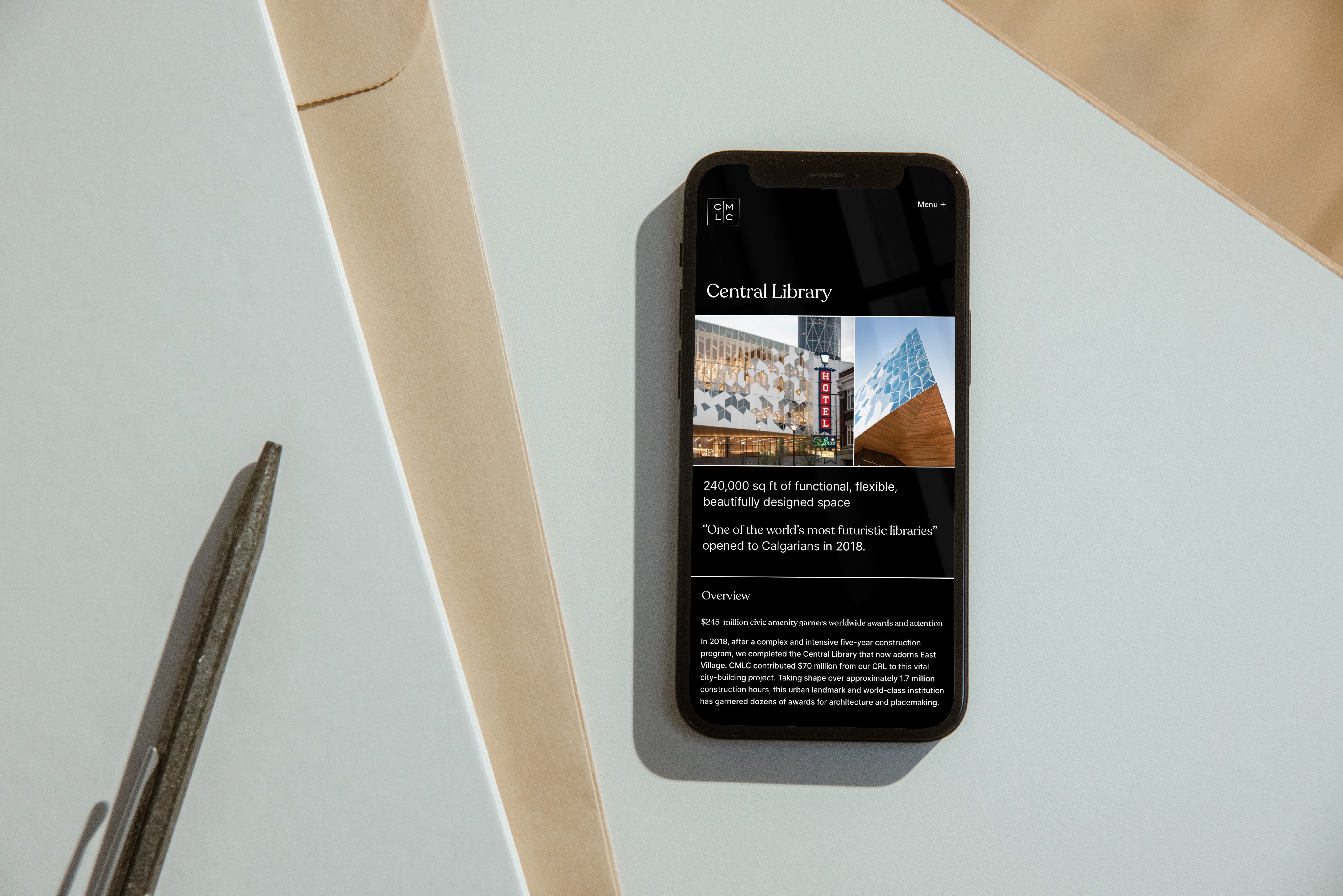 iPhone on a pale surface displaying the CMLC 'Central Library' page, with architectural photos and the line 'One of the world's most futuristic libraries.'