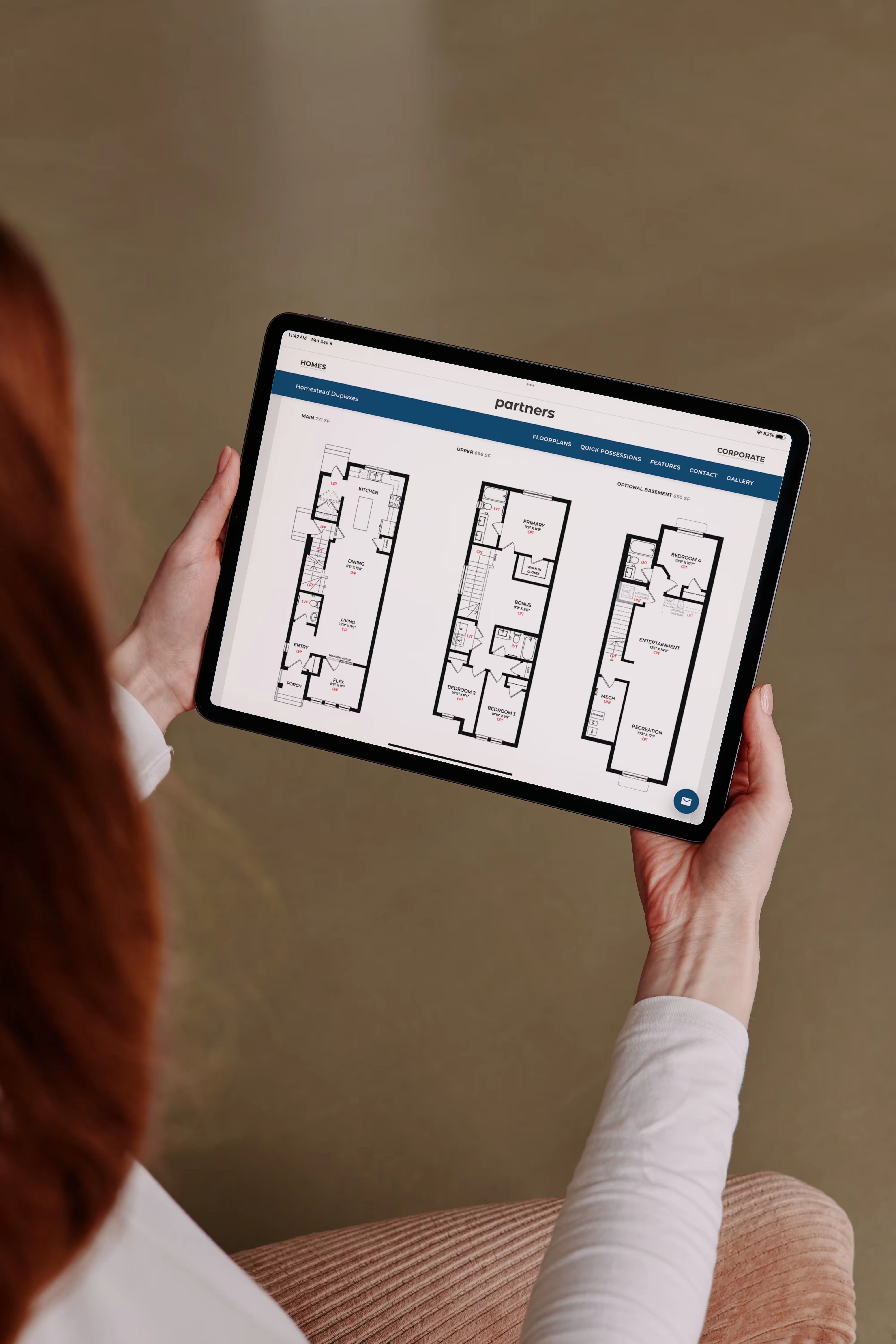 A person holding a tablet that shows three floor plans on the Partners Development Group website.