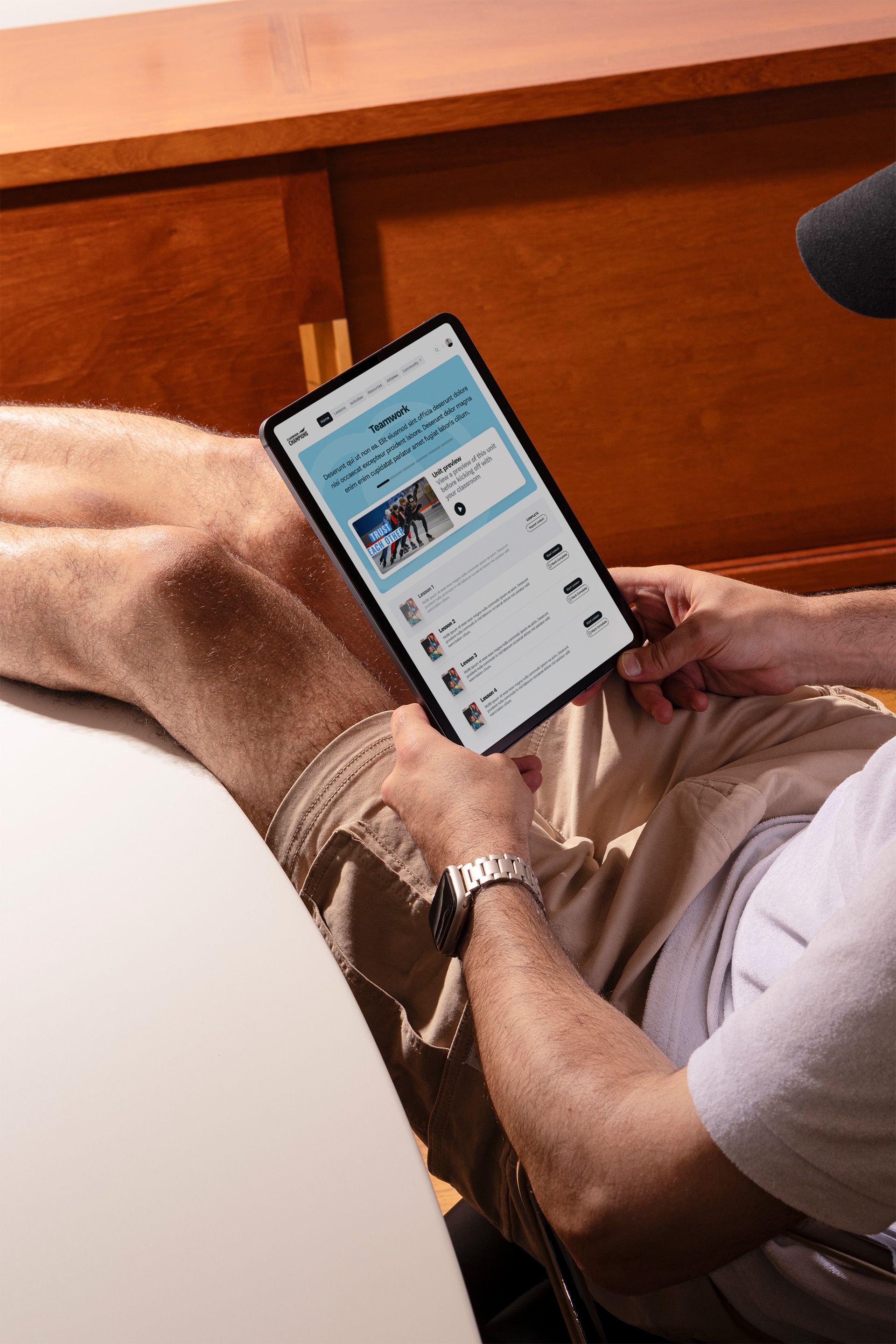 Overhead photo of a man seated on a leather chair holding a tablet that displays a 'Teamwork' lesson page from an online learning site.