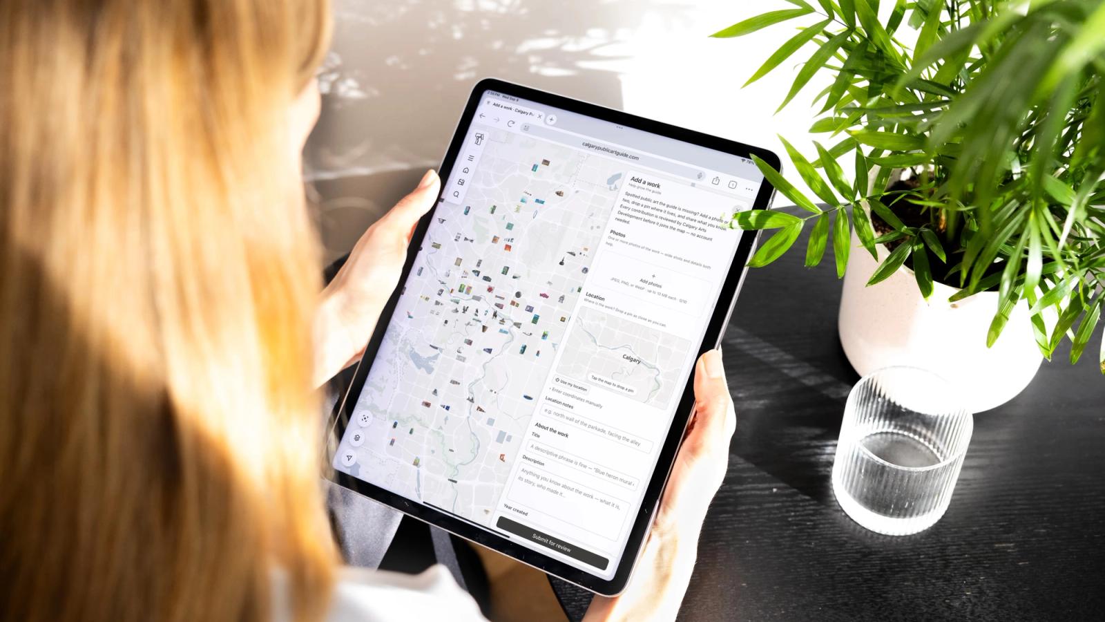 A person holding a tablet showing the Calgary Public Art Guide map beside a potted plant.
