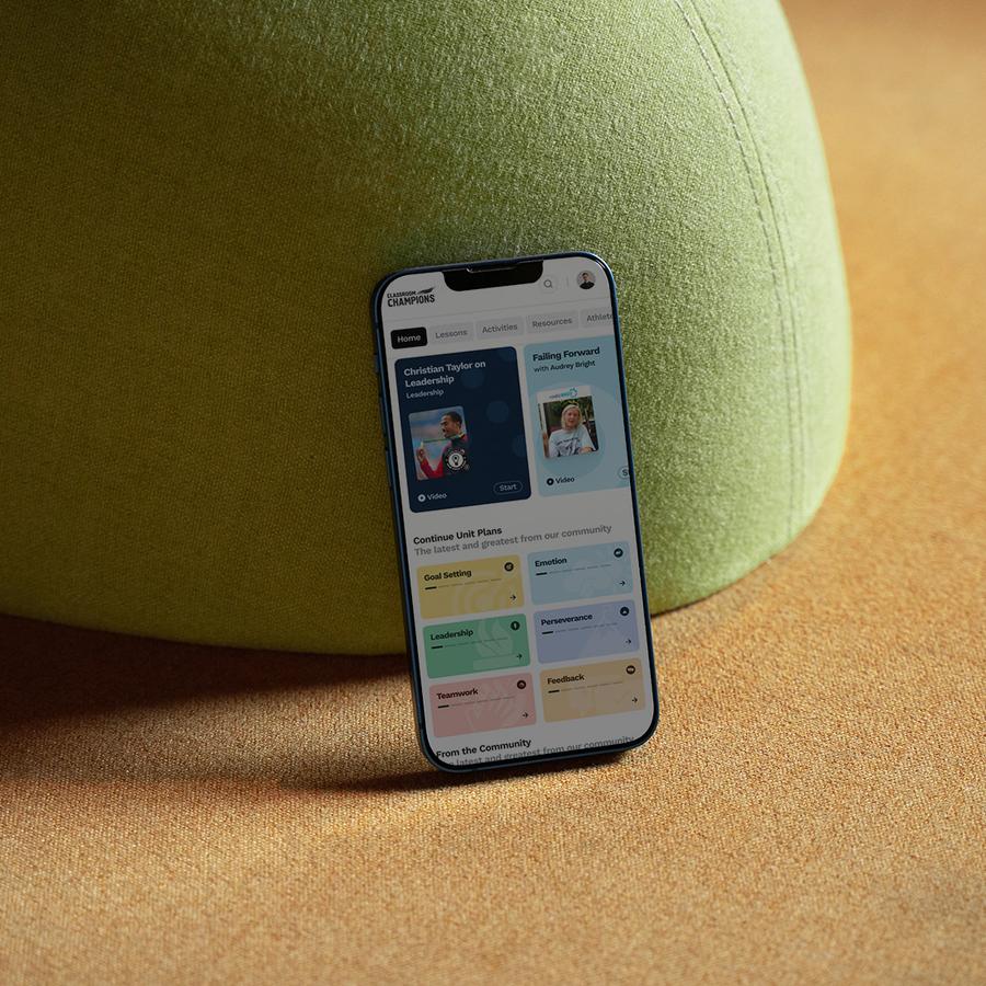 A phone showing the Classroom Champions teacher dashboard, propped against a green cushion.