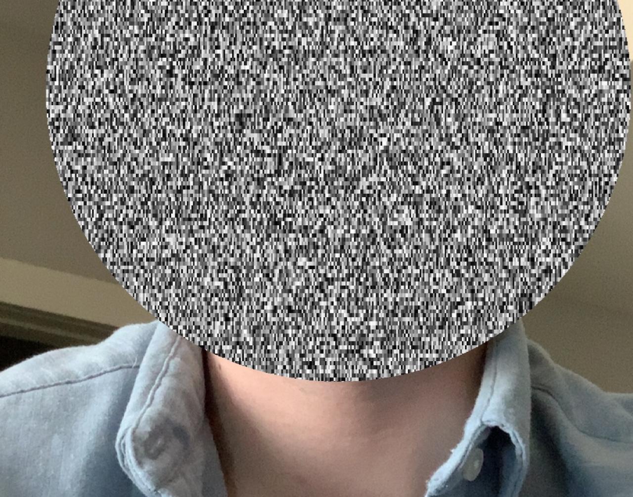 A man in a denim shirt whose face is covered by a circle of television static.