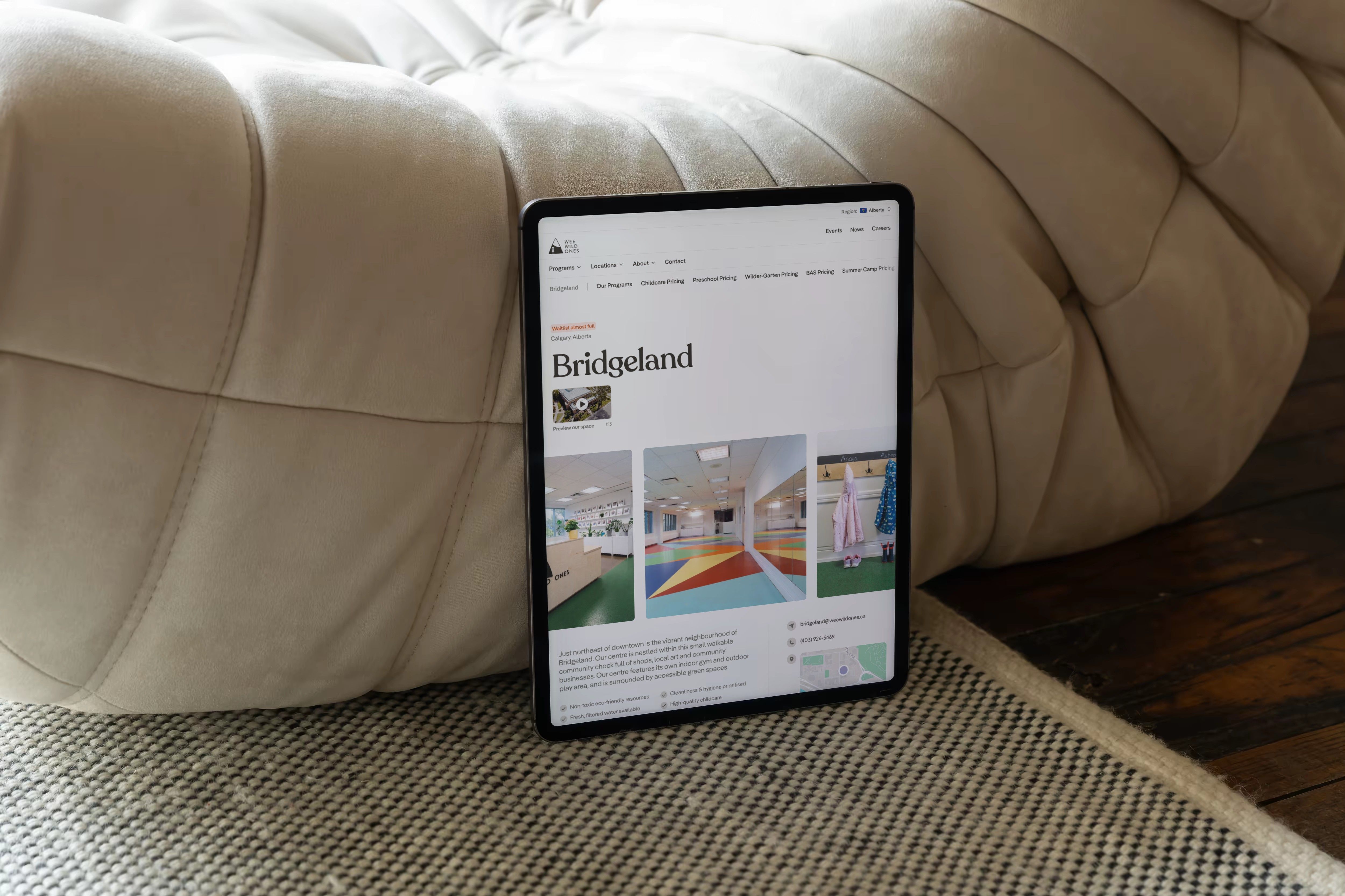 The Wee Wild Ones Bridgeland location page on a tablet, leaning against a cream leather pouf.