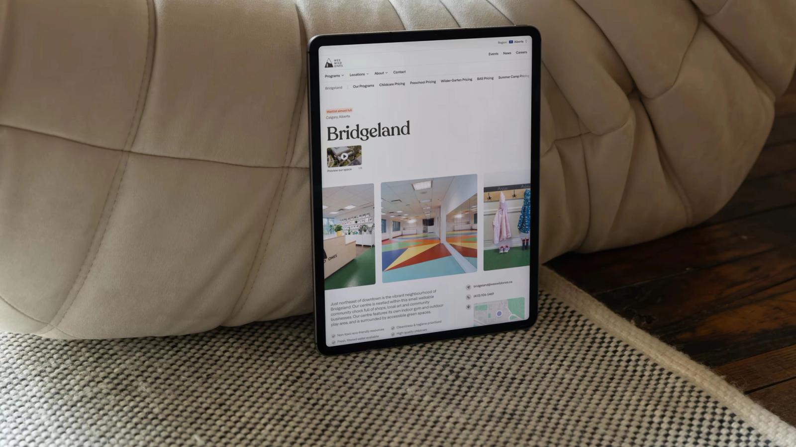 The Wee Wild Ones Bridgeland location page on a tablet, leaning against a cream leather pouf.