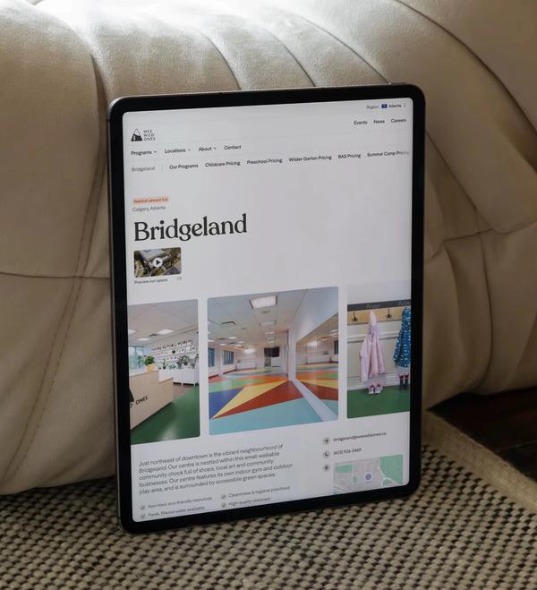 The Wee Wild Ones Bridgeland location page on a tablet, leaning against a cream leather pouf.