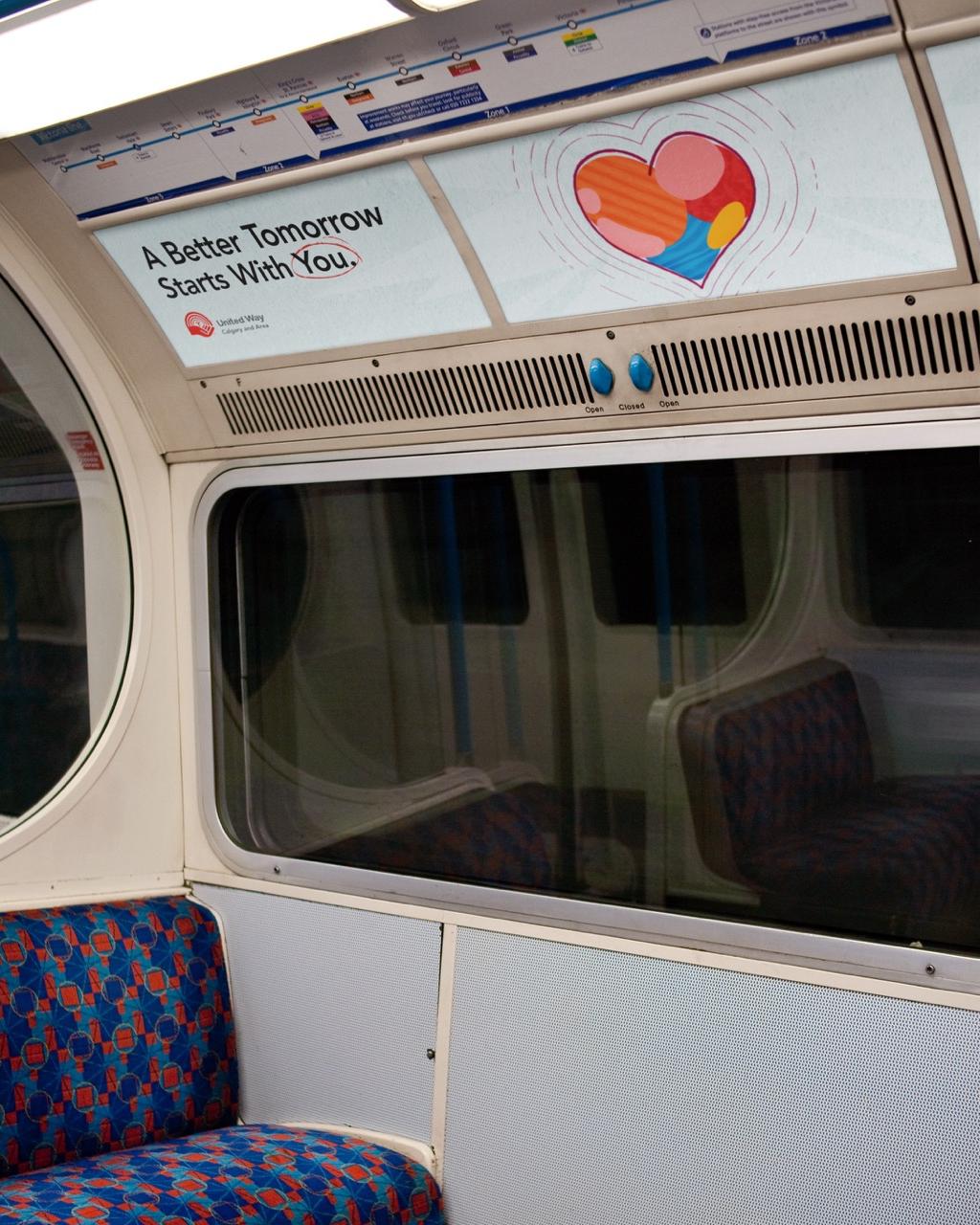 The inside of a train car looking at a seating bench with an advertisement with a heart and text saying "A Better Tomorrow Starts With You" above.