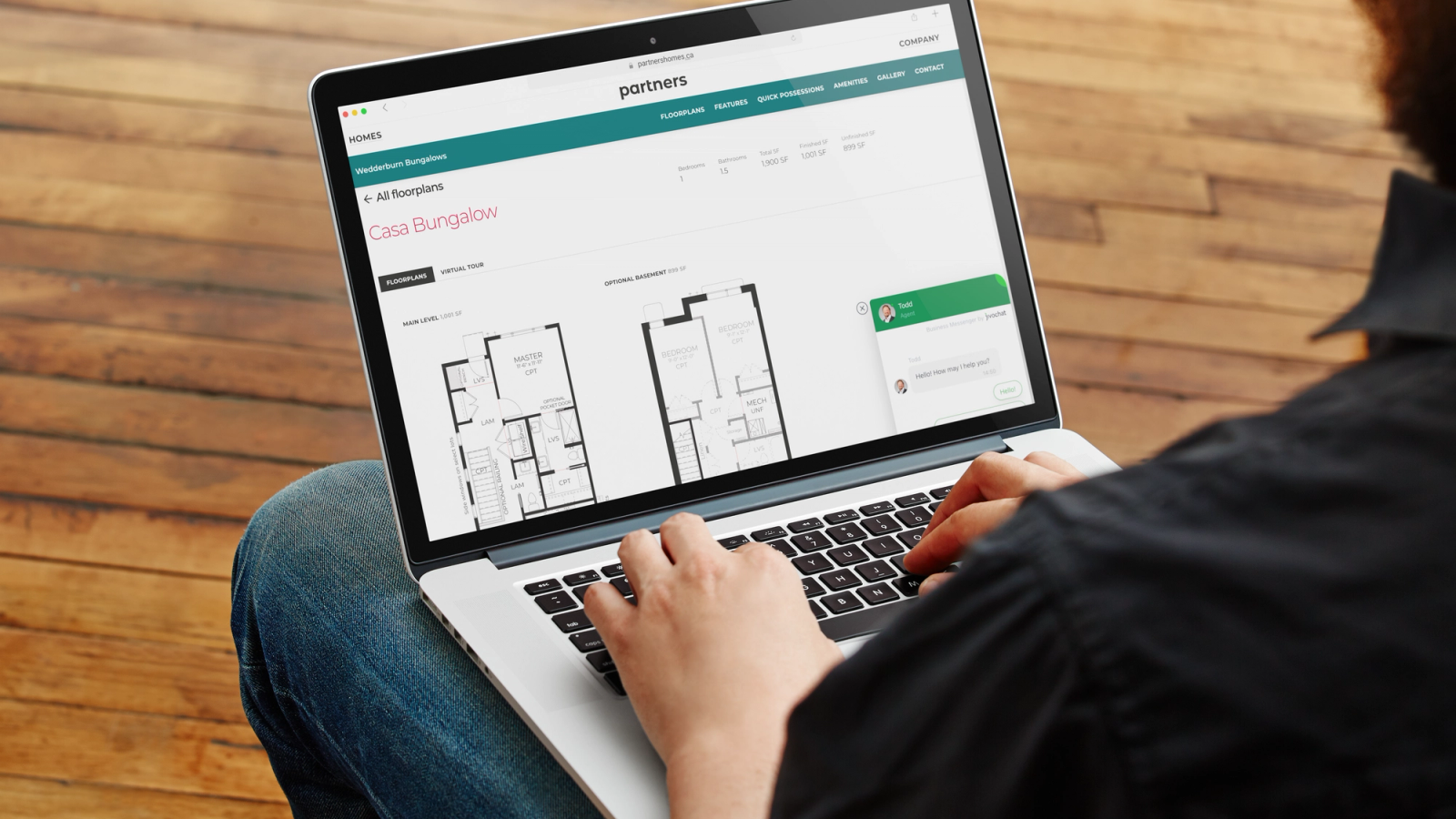 A person using a laptop that shows a bungalow floor plan page on the Partners Development Group website.