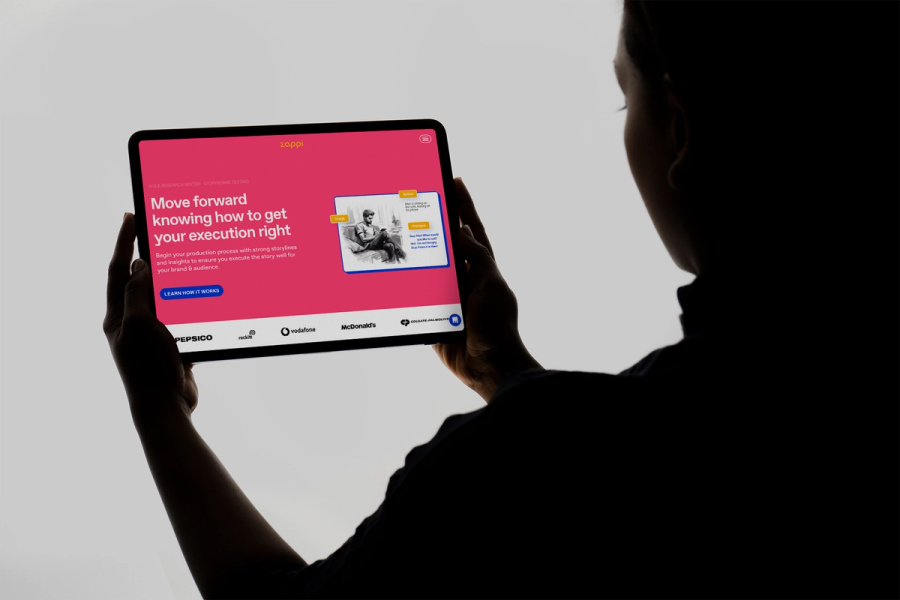 Person in silhouette holding an iPad that displays a pink Zappi website page headlined 'Move forward knowing how to get your execution right.'