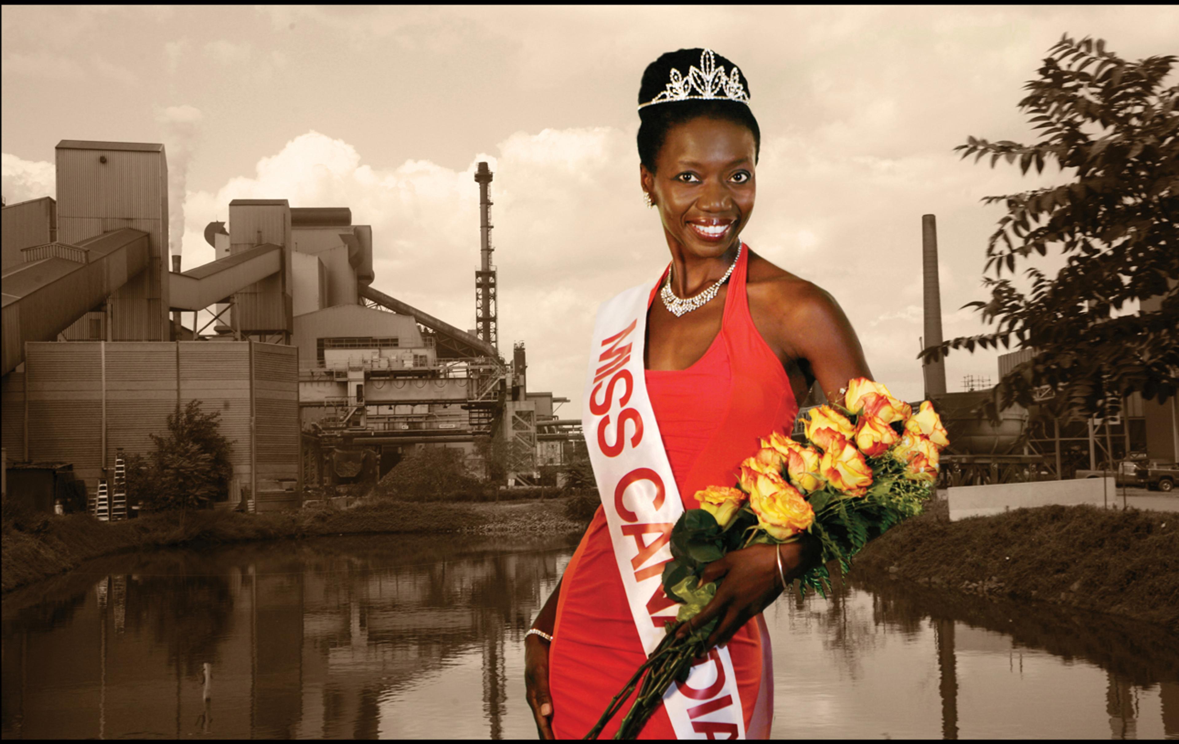 Black woman in a long red gown wears a Miss Canadiana sash against an industrial background.