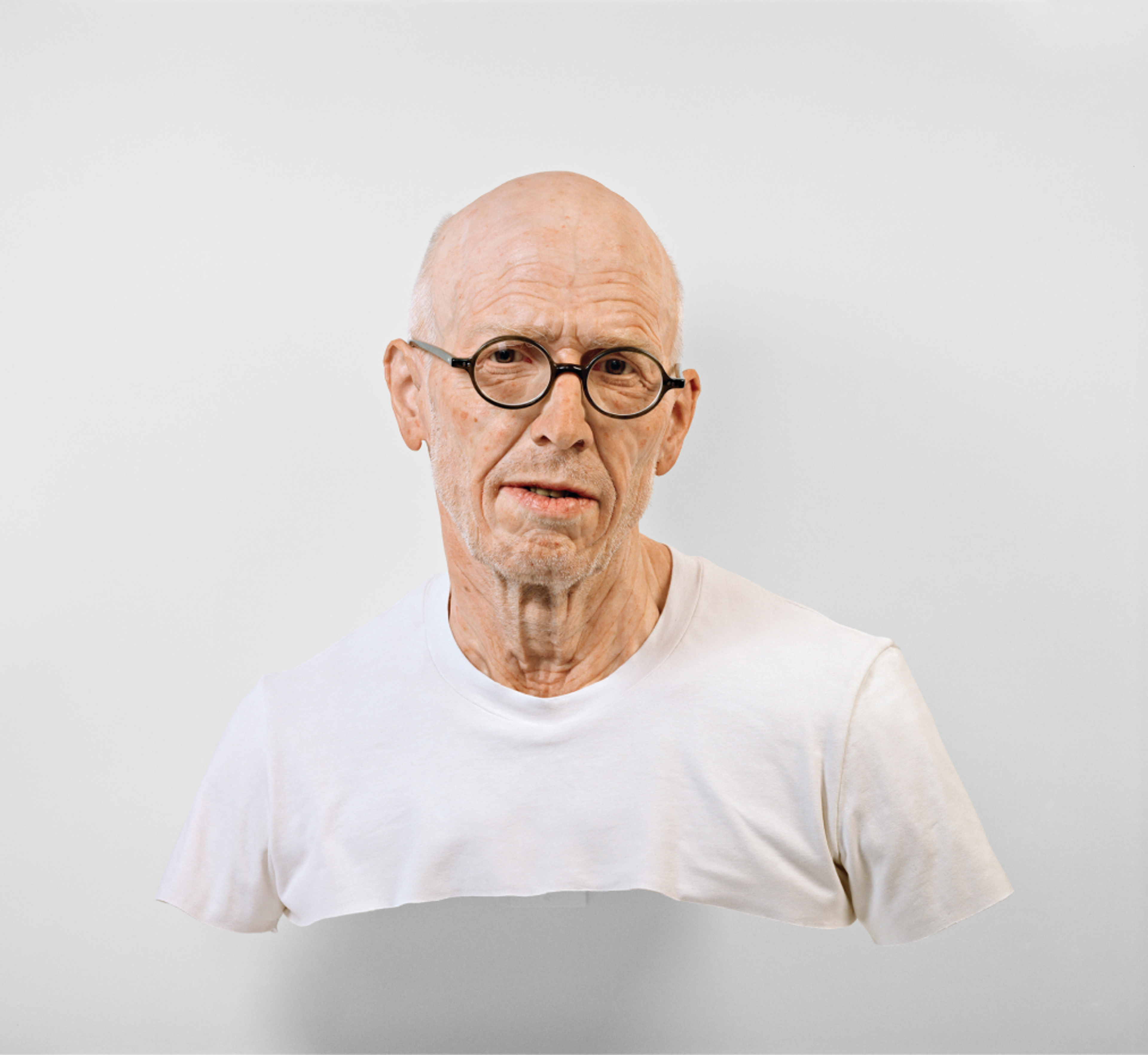 Sculpture of a realistic looking old man with black glasses in a white tshirt