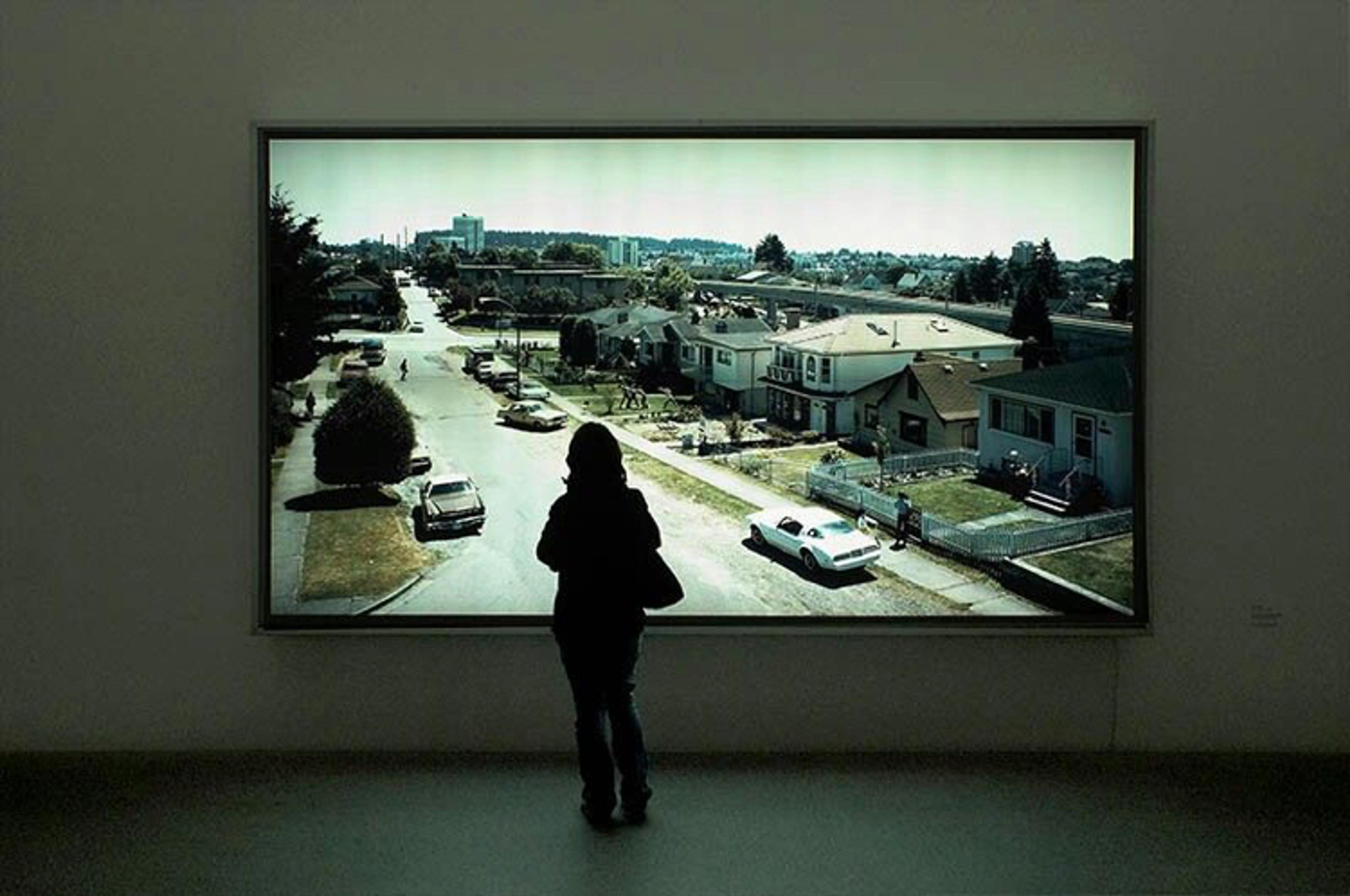 Person in front of a Jeff Wall lightbox standing in a dark gallery.