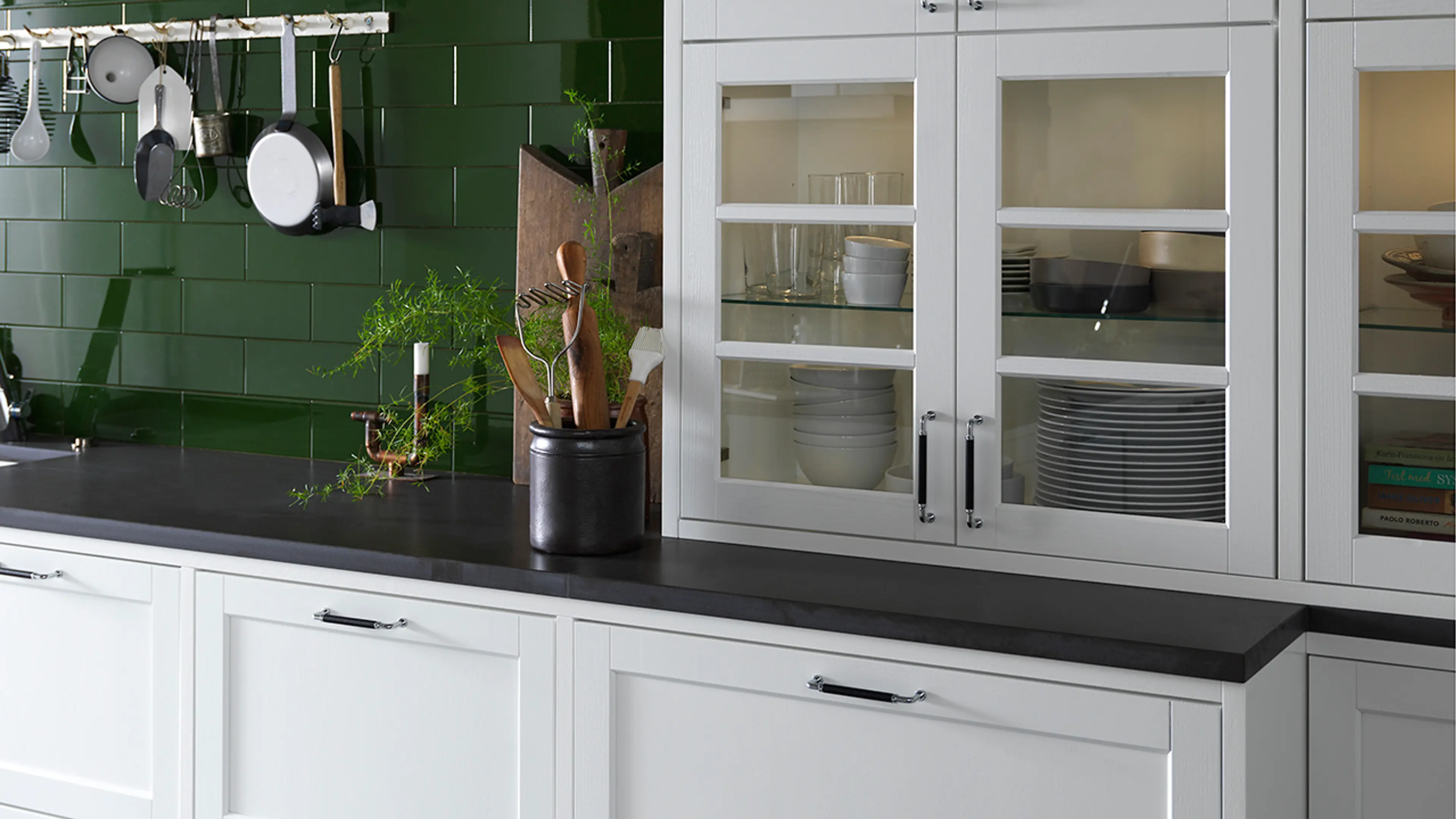 Detaljbilde av sort enkeplate til hvitt kjøkken med grønne flisvegger.
